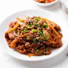 Délicieux boeuf aux oignons, garni de graines de sésame et de ciboule, servi sur une assiette blanche.