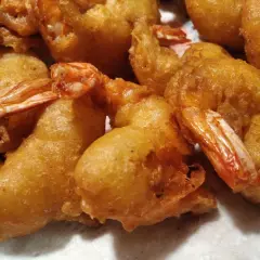 Gros plan sur des beignets de crevette dorés et croustillants, prêts à être dégustés. Les queues des crevettes dépassent de la pâte.