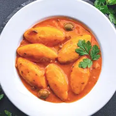 Assiette de quenelles de brochet en sauce tomate, garnie de persil et d'olives.