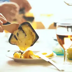 Raclette fondue dégoulinant sur des pommes de terre, un verre de Bourgogne Aligoté à côté.