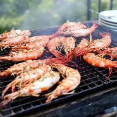Grosses gambas barbecue sur un grill, fumant et appétissant. Les crevettes sont bien caramélisées, prêtes à être dégustées.