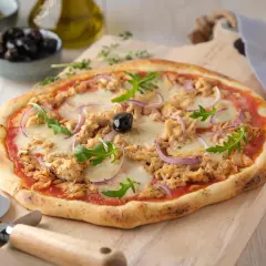 Une délicieuse pizza au thon, garnie d'oignons rouges, de roquette et d'une olive noire, prête à être découpée.