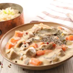 Un plat de blanquette de veau crémeuse avec des carottes et des champignons, servi avec du riz. Un verre de vin rouge est suggéré pour accompagner ce délice.