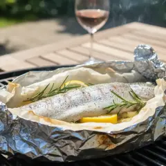 Une truite au barbecue, enveloppée dans du papier d'aluminium avec du citron et du romarin, fume doucement sur la grille.