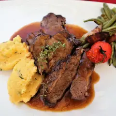 Savoureux sabodet au vin rouge, servi avec une polenta crémeuse, des haricots verts enroulés de lard et une tomate confite.