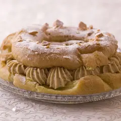 Un Paris-Brest garni d'une généreuse crème mousseline praliné, saupoudré de sucre glace et d'éclats de noisettes.