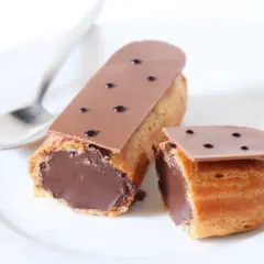 Deux éclairs au chocolat, un entier et un coupé, sur une assiette blanche avec une cuillère. Parfait pour une recette éclair au chocolat.