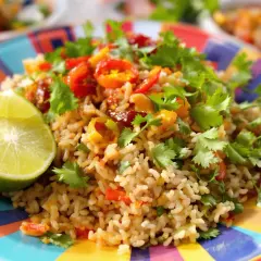 Un plat coloré de riz frit thaï, garni de coriandre fraîche et de quartiers de citron vert, sur une assiette vibrante.