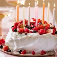 Pavlova fruit rouge, ornée de fraises, framboises et myrtilles, avec des bougies allumées pour une fête gourmande.