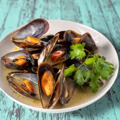 Un plat de moules au roquefort, garni de persil frais, baignant dans une sauce crémeuse. Un délice savoureux sur une table en bois bleu délavé.