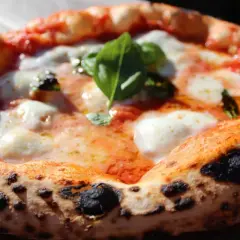 Une pizza napolitaine authentique, avec sa croûte gonflée et tachetée, garnie de sauce tomate, mozzarella fondante et basilic frais. La recette parfaite pour un délice italien.