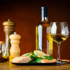 Un plat de saumon avec citron et persil, accompagné d'une bouteille et d'un verre de bon vin blanc sec, d'une salière, d'une poivrière et d'une burette d'huile d'olive.