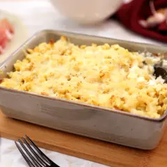Un plat de gratin de crozet doré et gratiné, prêt à être dégusté. Une assiette de jambon cru est visible à gauche.