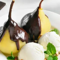 Poires pochées nappées de chocolat noir, servies avec de la glace à la vanille et des éclats de noisettes. Un délice de poire Belle Hélène.