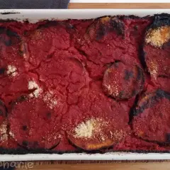Un plat de parmigiana di melanzane tout juste sorti du four, avec des bords légèrement caramélisés et une sauce tomate savoureuse.