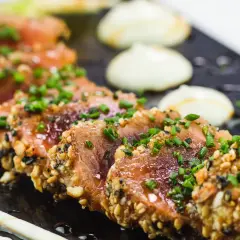 Tataki de thon en croûte de sésame et noix, garni de ciboule fraîche. Un accompagnement visuellement appétissant.