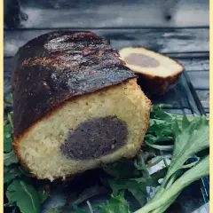 Un délicieux saucisson brioché, coupé en deux, repose sur un lit de verdure. Sa croûte dorée et sa mie moelleuse invitent à la dégustation.