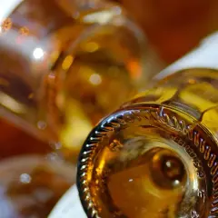 Gros plan sur le goulot d'une bouteille de vin ambré, évoquant un sauterne sec ou moelleux. Reflets lumineux sur le verre.