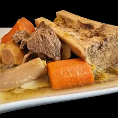 Un plat généreux de pot-au-feu cocotte minute : viande, os à moelle, carottes et poireaux mijotés dans un bouillon savoureux.