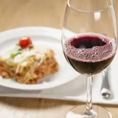 Un verre de vin rouge pétillant à côté d'une assiette de lasagnes au fromage fondu. La question est : quel vin avec des lasagnes ?