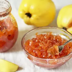 Confiture de coings sans les peler, servie dans un bocal et un bol, avec des coings entiers et une tranche en arrière-plan.