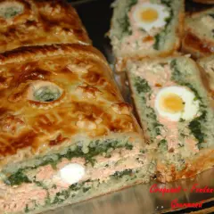 Un koulibiac de saumon doré, garni d'épinards et d'œufs durs, est coupé en tranches appétissantes.