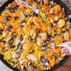 Un plat généreux de riz façon paella, garni de crevettes, moules et morceaux de poulet, prêt à être dégusté.