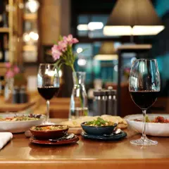 Verre de vin rouge tannique et puissant, accompagné de plats appétissants et d'une touche florale, dans une ambiance de restaurant chaleureuse.