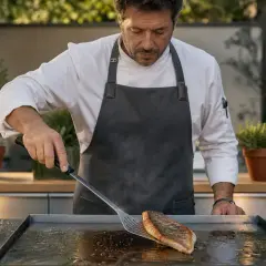 Un chef prépare un poisson sur un **bar à la plancha** en extérieur. L'arôme du poisson grillé embaume l'air.