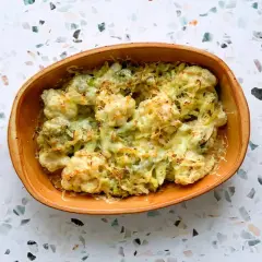 Un délicieux gratin chou-fleur brocolis, gratiné au fromage, servi dans un plat en terre cuite. Quelques fleurons frais entourent le plat.