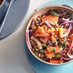 Salade de lentilles savoureuse avec du saumon fumé, des tomates et des oignons rouges, garnie de persil frais.