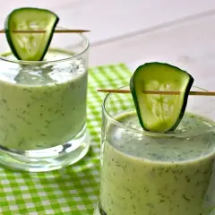 Deux verres de gaspacho concombre, décorés d'une tranche de concombre sur un cure-dent, sur une nappe à carreaux verts.