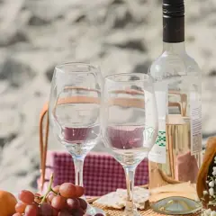 Un pique-nique sur la plage avec des verres, des raisins et une bouteille de vin. Idéal pour savoir comment choisir un vin rosé parfait pour l'occasion.