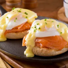 Deux oeufs Bénédicte au saumon fumé, nappés de sauce hollandaise et parsemés de ciboulette, servis sur un muffin anglais dans une poêle.