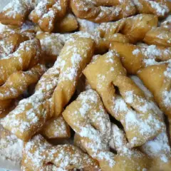 Une assiette généreuse de bugnes lyonnaises dorées, saupoudrées de sucre glace. La meilleure recette de bugnes lyonnaises pour un goûter gourmand.