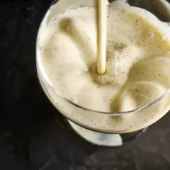 Une crème anglaise onctueuse, parsemée de points de vanille, est versée dans un verre.