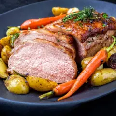 Délicieuse côte de veau barbecue, tranchée et servie avec des pommes de terre rôties et des carottes glacées, garnie d'herbes fraîches.