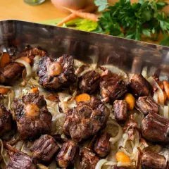 Morceaux de queue de bœuf rôtis dans un plat avec des oignons et des carottes. Un plat savoureux, parfait pour un fond de veau riche.