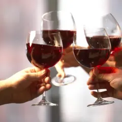 Quatre mains portent des verres de vin rouge pour un toast. Une belle façon de célébrer et de savoir comment boire du vin rouge.