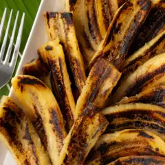 Bananes flambées grillées sur une feuille de bananier, prêtes à être dégustées avec deux fourchettes.
