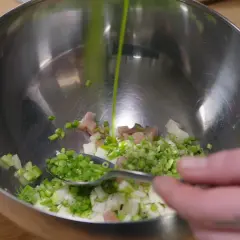 Préparation d'une salade nordique : on verse une sauce verte sur des dés de poisson, oignons et aneth dans un bol.