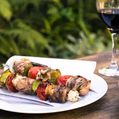 Brochettes de viande et légumes grillés, accompagnées d'un verre de vin pour grillade et d'un bol de pain.