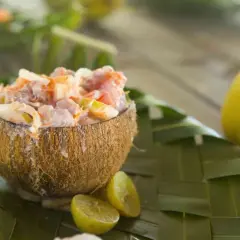 Salade tahitienne crémeuse servie dans une noix de coco, garnie de citron vert et de feuilles de palmier.