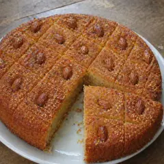 Un délicieux gâteau arabe au miel, parsemé d'amandes et de graines, coupé en carrés sur une assiette blanche.