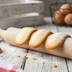 Délicieuses langues de chat saupoudrées de sucre glace, posées sur un rouleau à pâtisserie en bois.