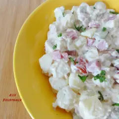 Salade piémontaise maison crémeuse, avec pommes de terre, jambon, tomates et persil, servie dans un plat jaune vif.