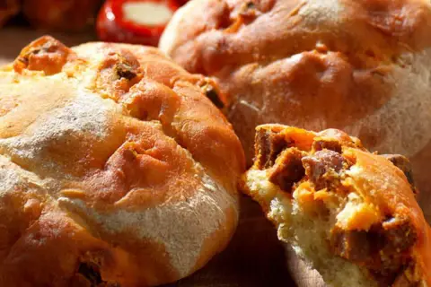 Gros plan sur des pains au chorizo dorés et croustillants, certains entiers, un autre coupé révélant la garniture savoureuse.