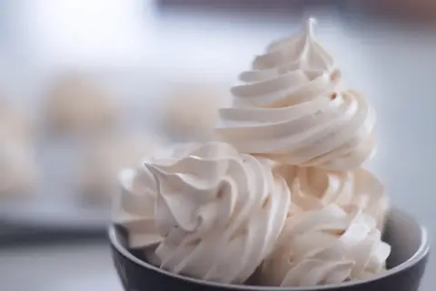 Un bol rempli de délicieuses meringues suisses, légères et aériennes, prêtes à fondre en bouche.