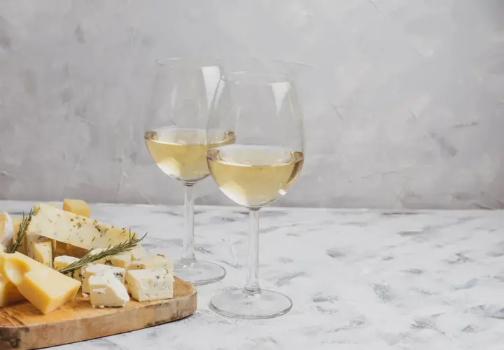 Deux verres de vin blanc pétillant, accompagnés d'une sélection de fromages sur une planche en bois.