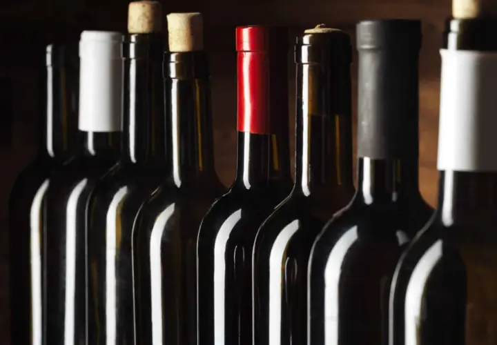 Une rangée de bouteilles de vin rouge, certaines avec des capsules de différentes couleurs, pour vous aider à comment reconnaître un bon vin rouge.